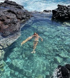 a man swimming in clear blue water next to rocky shore with rocks on both sides