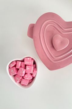 pink candy cubes in a heart shaped bowl next to a ceramic container with lid