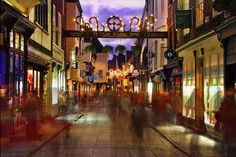 people are walking down the street in front of shops at night with lights on them