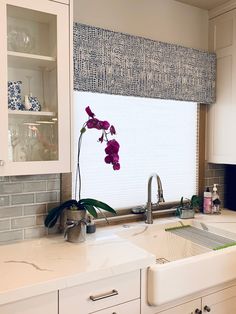 a kitchen with white cabinets and purple flowers on the window sill above the sink