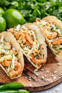 three shrimp tacos on a wooden cutting board with limes and seasoning in the background