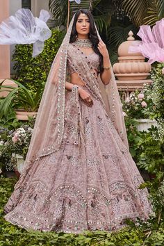 a woman in a pink lehenga with an umbrella on her head and flowers behind her