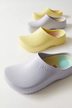 three pairs of white and yellow clogs sitting on top of a table next to each other