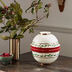 a white vase sitting on top of a wooden table next to a bowl filled with berries