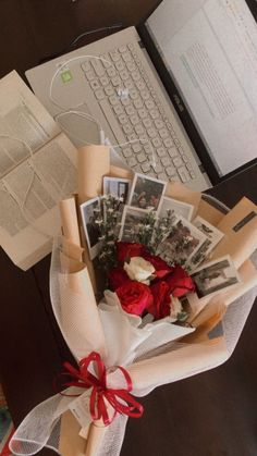 a bouquet of flowers and pictures on a desk next to a laptop computer with papers wrapped around it