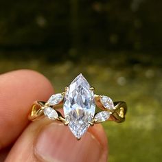 a person holding an engagement ring with three pear shaped diamonds on the band and side stones