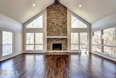 an empty living room with large windows and a stone fire place in the middle of it