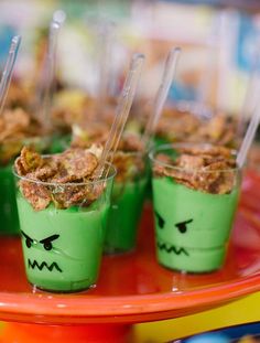 desserts with green frosting and candy eyes on them are displayed in plastic cups