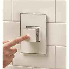 a person is pressing the light switch button on a white tile wall with their finger