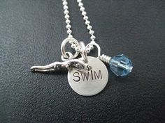 a silver necklace with a blue crystal bead hanging from it's end and the word swim on it