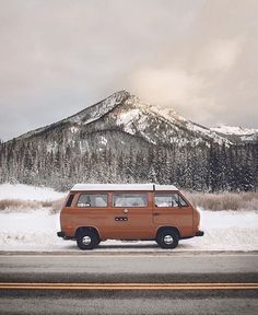 an orange van is parked on the side of the road in front of a mountain