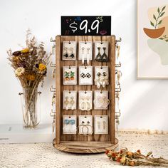 a wooden display case with earrings hanging on it's sides and flowers in the background