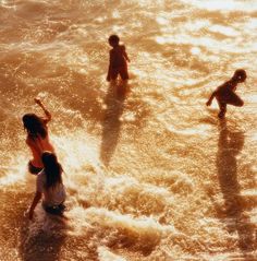 three children playing in the ocean at sunset