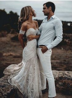 a man and woman standing next to each other on top of a rocky cliff near the ocean