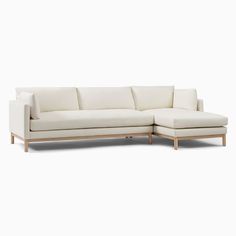 a white sectional couch with wooden legs and pillows on it's left side, facing the camera