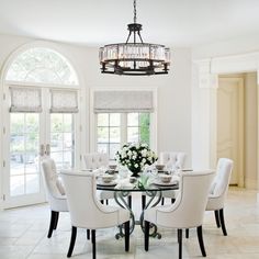 a dining room table with white chairs and a chandelier hanging from the ceiling