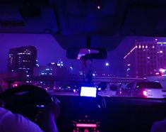 two people in a car driving at night with the city lights on and buildings lit up behind them