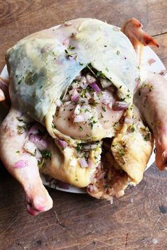 a whole chicken covered in sauce and herbs on a white plate sitting on a wooden table