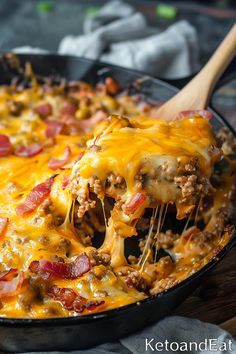 a casserole dish with meat and cheese being lifted from the skillet by a wooden spoon