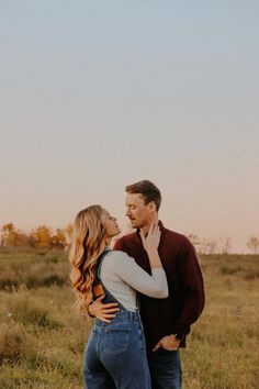 a man and woman standing in the middle of a field with their arms around each other