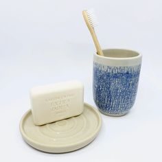 a blue and white cup with a toothbrush in it next to a soap dish