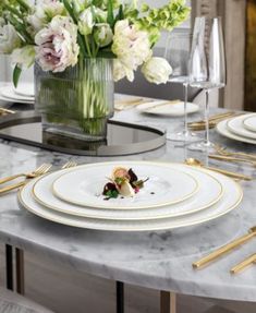 the table is set with white and gold place settings, silverware, and flowers