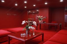 a room with red couches, tables and flowers in vases on the coffee table