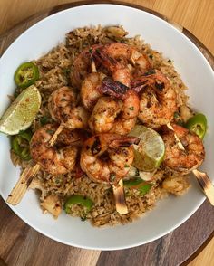 a white plate topped with shrimp, rice and limes on top of a wooden table