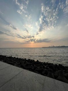 the sun is setting over the ocean with clouds in the sky