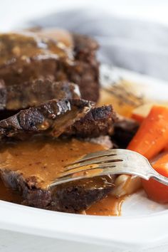 a plate with meat, carrots and gravy on it next to a fork