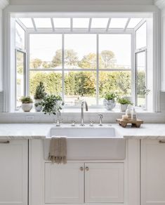 a white kitchen with large windows and lots of potted plants in the window sill