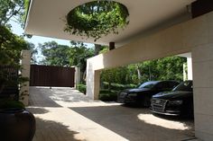 two cars parked in front of a house with trees on either side and an open driveway