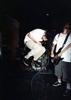 two young men are playing guitars in the dark