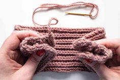 two hands are holding up a crocheted object with yarn and scissors in it