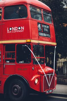 a red double decker bus driving down the street with people on it's side