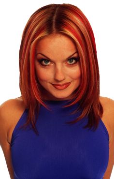 a woman with red hair and blue top posing for the camera in front of a white background