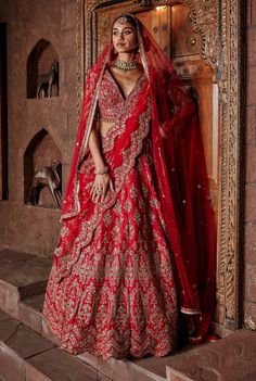 a woman in a red and gold bridal gown posing for the camera with her hands on her hips