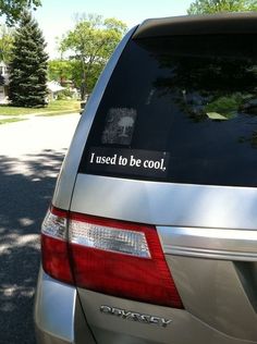 the back end of a silver car parked in a parking lot with trees behind it