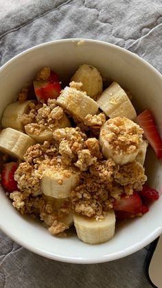 a white bowl filled with fruit and crumbs on top of a gray cloth