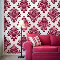 a red couch sitting in front of a wall with a large flower pattern on it