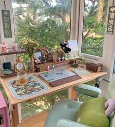 a desk with lots of stuff on it in front of a window and some plants