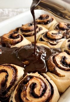 chocolate sauce being poured on top of cinnamon rolls