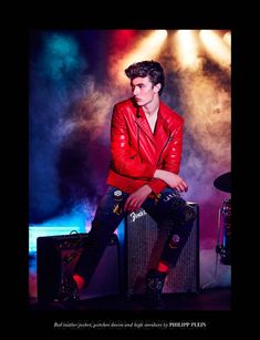 a young man sitting on top of a guitar amp in front of a stage light