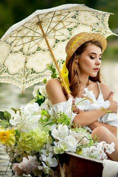 a woman sitting in a boat with an umbrella over her head and flowers on the side