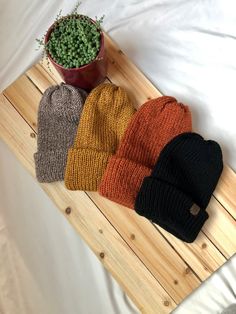 three knit beanies sitting on top of a wooden tray next to a potted plant