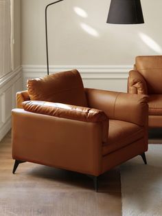 a brown leather chair sitting next to a lamp on a wooden floor in front of a white wall