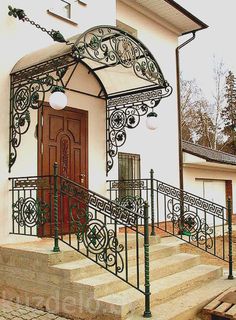 a white house with wrought iron railings and lights on the front door, next to a tree