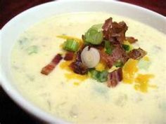 a bowl of soup with bacon, cheese and green onions on it sitting on a table