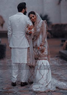 a man and woman dressed in white standing next to each other on a cobblestone walkway