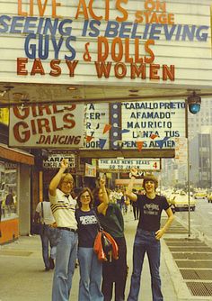 three women standing on the sidewalk in front of a theater sign that says, live acts sing seeing is believing guys & dolls easy and women